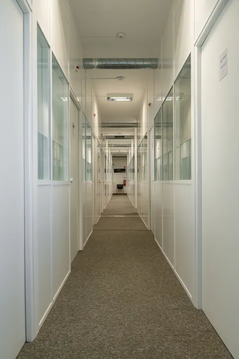 Corredor com divisórias brancas e portas de vidro.